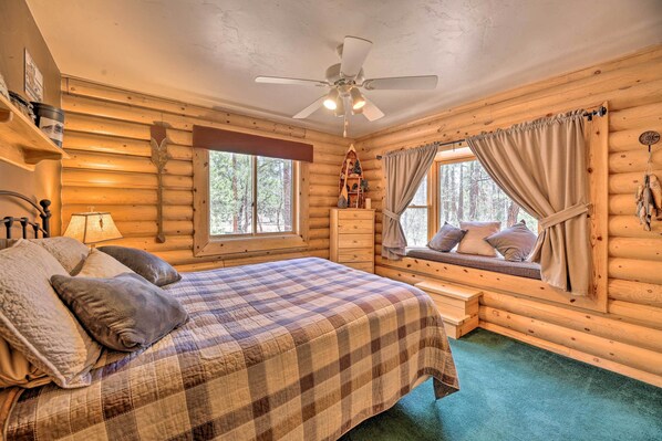 A cozy log cabin bedroom with a bed, a window seat, a ceiling fan, and a dresser. - 2-acre Cabin in Pinetop-lakeside w/ Fenced Yard (Lakeside)