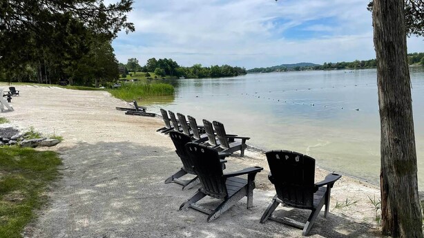 Un espace au bord du lac, agrémenté de plusieurs fauteuils Adirondack disposés le long d’un chemin de gravier.