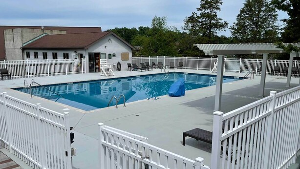 A swimming pool with a white fence, a covered seating area, and a building in the background. - Modern-chic Athens Home - Fish, Ski & Swim! (Athens)