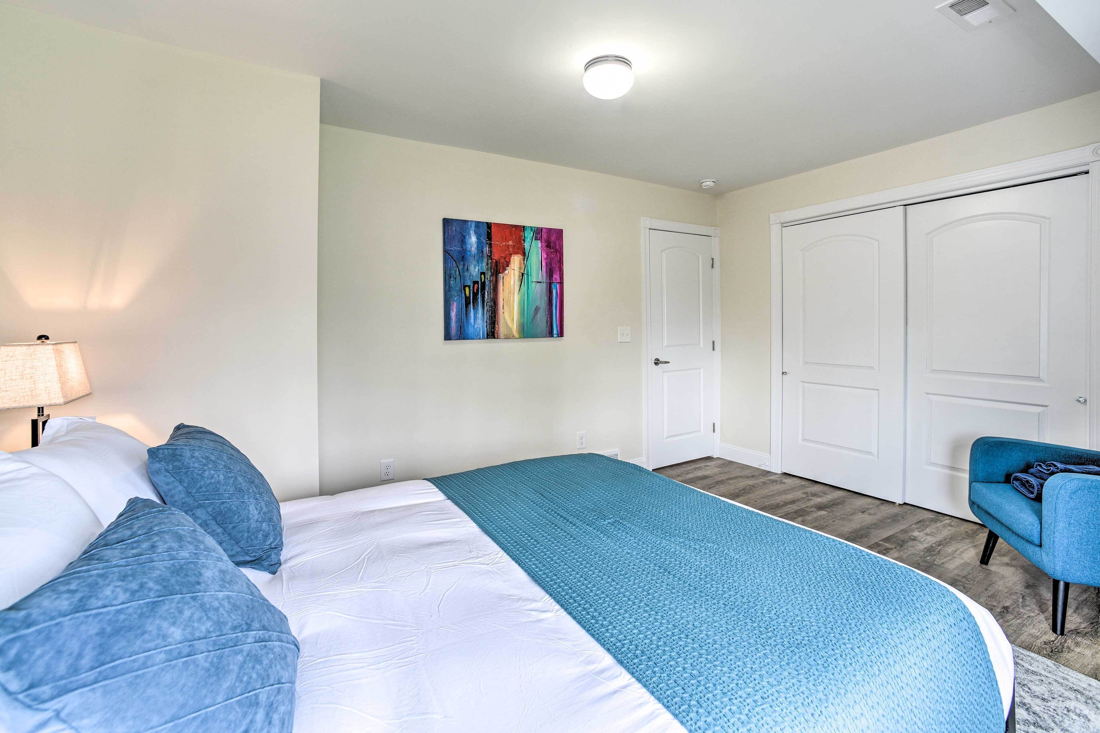 A bedroom with a bed, a blue blanket, a colorful painting on the wall, and a closet.