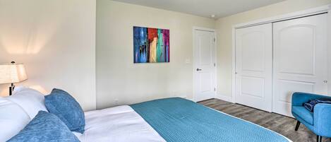 A bedroom with a bed, a blue blanket, a colorful painting on the wall, and a closet.