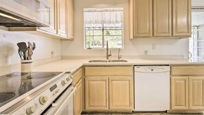 A kitchen with wooden cabinets, a stainless steel stove, a dishwasher, and a window with a lace curtain. - Phoenix Desert Getaway: Pool, Grill & EV Charging! (Phoenix)