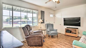 A living room with a large window, a ceiling fan, a television, and a sofa. - Phoenix Desert Getaway: Pool, Grill & EV Charging! (Phoenix)