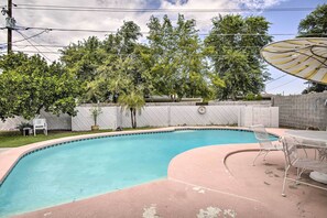 A swimming pool with a curved edge, surrounded by a concrete deck and metal chairs. - Phoenix Desert Getaway: Pool, Grill & EV Charging! (Phoenix)
