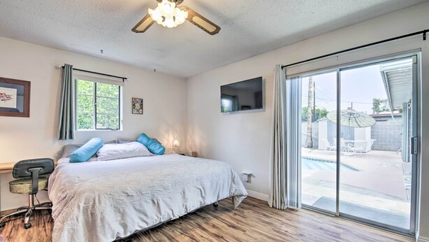 A bedroom with a bed, a desk, a chair, a ceiling fan, a TV, and a sliding glass door leading to an outdoor area with a pool. - Phoenix Desert Getaway: Pool, Grill & EV Charging! (Phoenix)