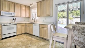 A kitchen with wooden cabinets, a microwave, an oven, and a dishwasher. There is a dining area with a table and chairs. - Phoenix Desert Getaway: Pool, Grill & EV Charging! (Phoenix)