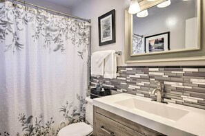 A bathroom with a floral shower curtain, a sink with a modern faucet, and a tiled backsplash. - Phoenix Desert Getaway: Pool, Grill & EV Charging! (Phoenix)