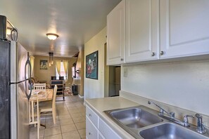 A kitchen with a refrigerator, double sink, wooden dining table, and white cabinets.