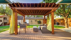 A covered patio with wicker furniture, a table, and a bench. - Lovely Lubbock Home w/ Furnished Deck & Grill (Lubbock)