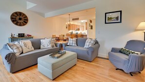 A living room with a grey sofa, a grey armchair, and a coffee table. There is a wooden clock on the wall and a framed picture on the wall.
