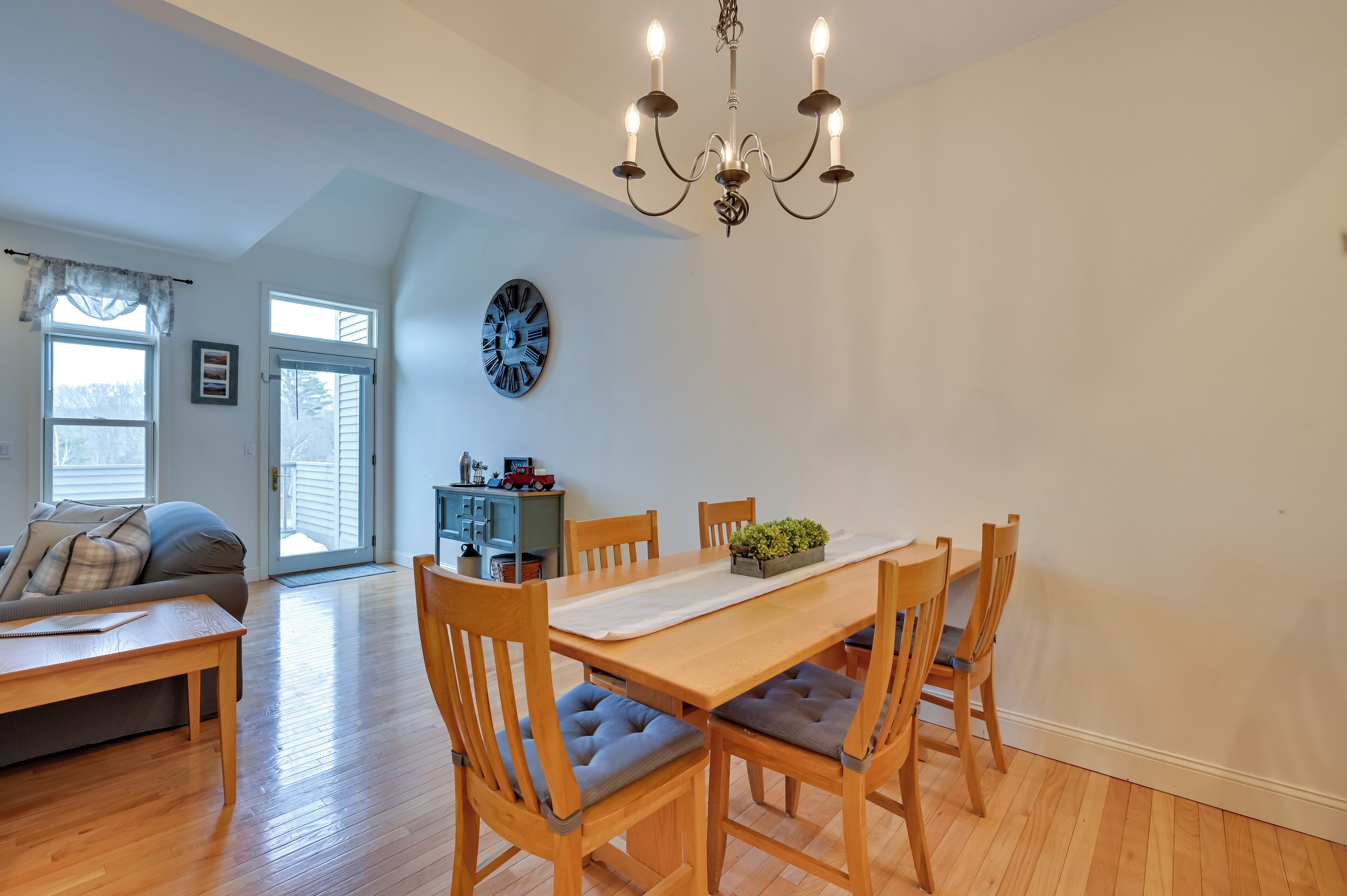 A dining area with a wooden table and chairs, a chandelier, and a view of the outdoors.
