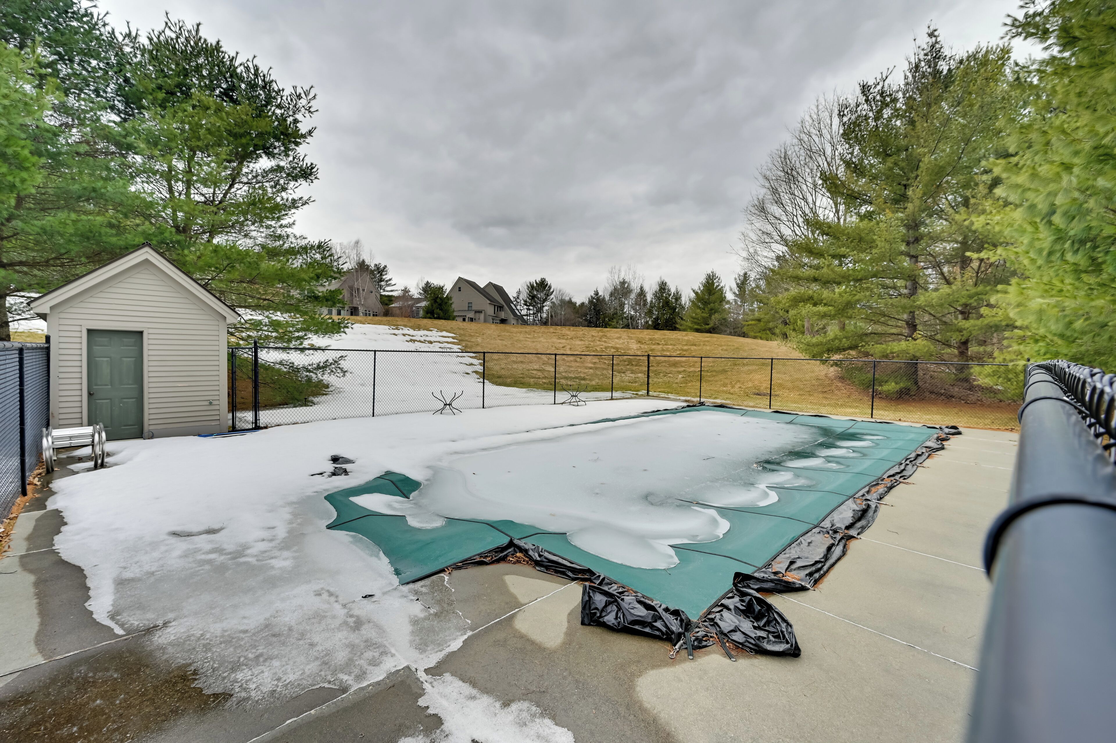 A backyard with a snow-covered patio and a green tarp.