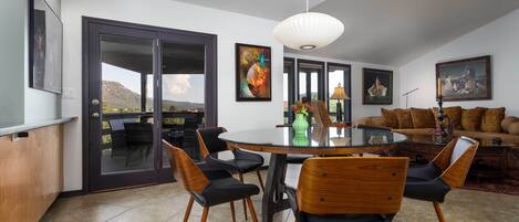 A spacious dining area with a round table, black and wooden chairs, and a view through glass doors to the outside.