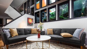 A modern living room with a sectional sofa, a round coffee table, and a staircase with large windows. - Outdoor Entertaining Space: Seonda Mtn-view Home (Sedona)