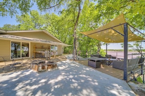 A covered outdoor patio with seating and a fire pit, overlooking a body of water.