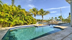 A clear pool with a tiled edge, surrounded by palm trees and a boat dock.