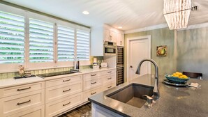 A modern kitchen with white cabinetry, a stainless steel sink, and a large window with blinds.