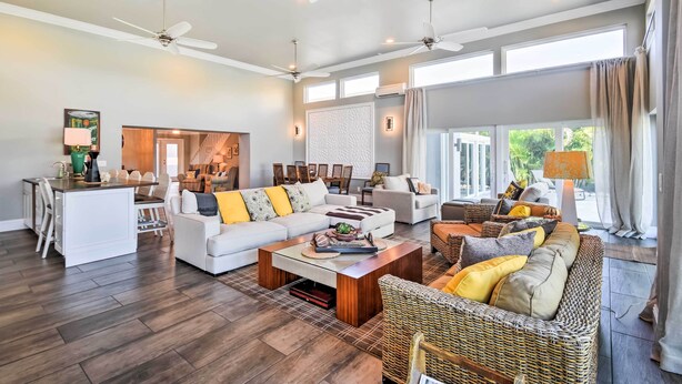 A spacious living area with a white sofa, a wicker sofa, and a dining area with a white table.