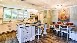 A modern kitchen with a central island, white cabinetry, and a dining area with a bench and chairs.