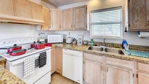 A kitchen with wooden cabinets, a white stove, a microwave, a sink, and a window with blinds. - Corpus Christi Extended Stay - 7 Mi to Beach! (Corpus Christi)