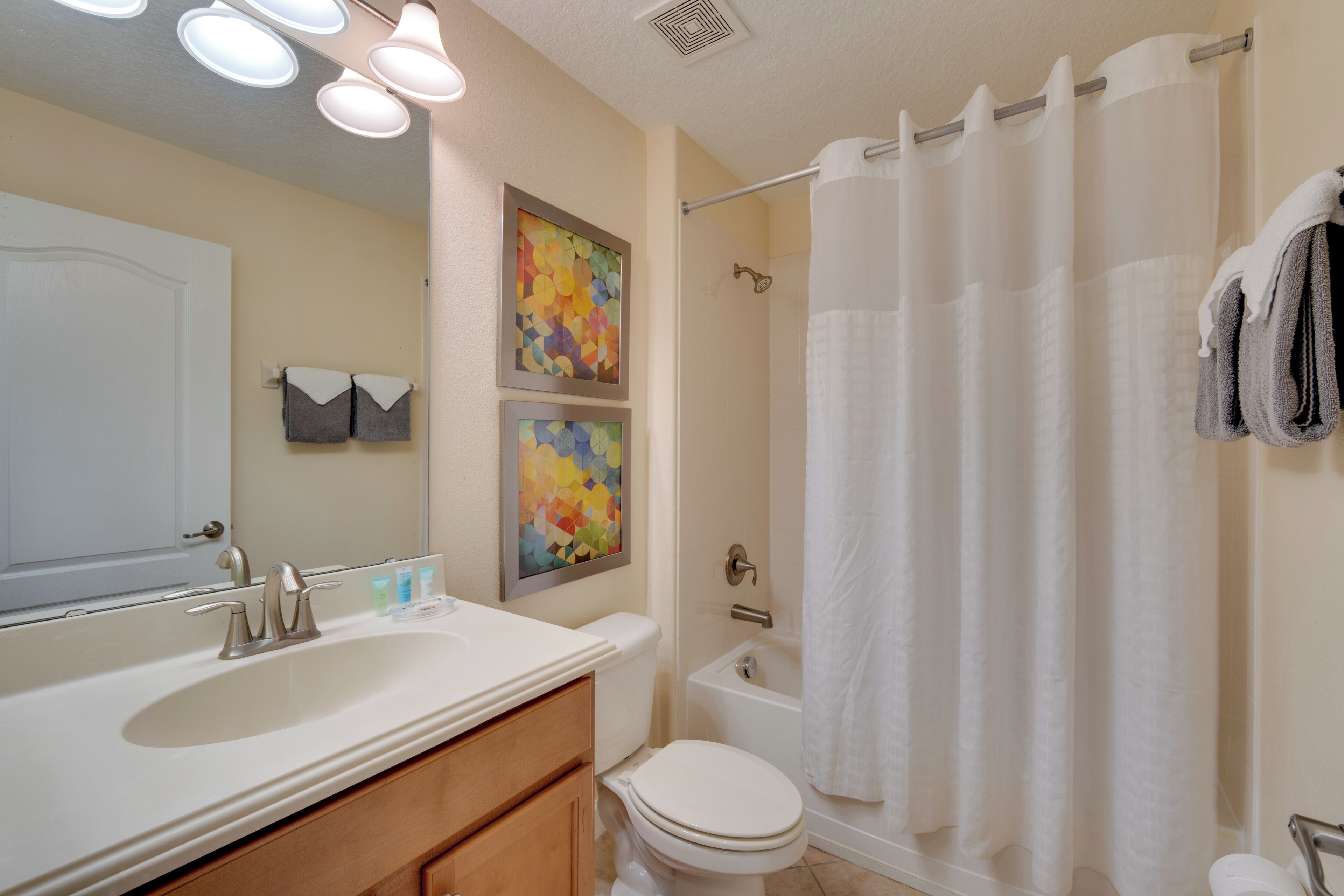 A bathroom with a sink, mirror, toilet, and shower curtain.