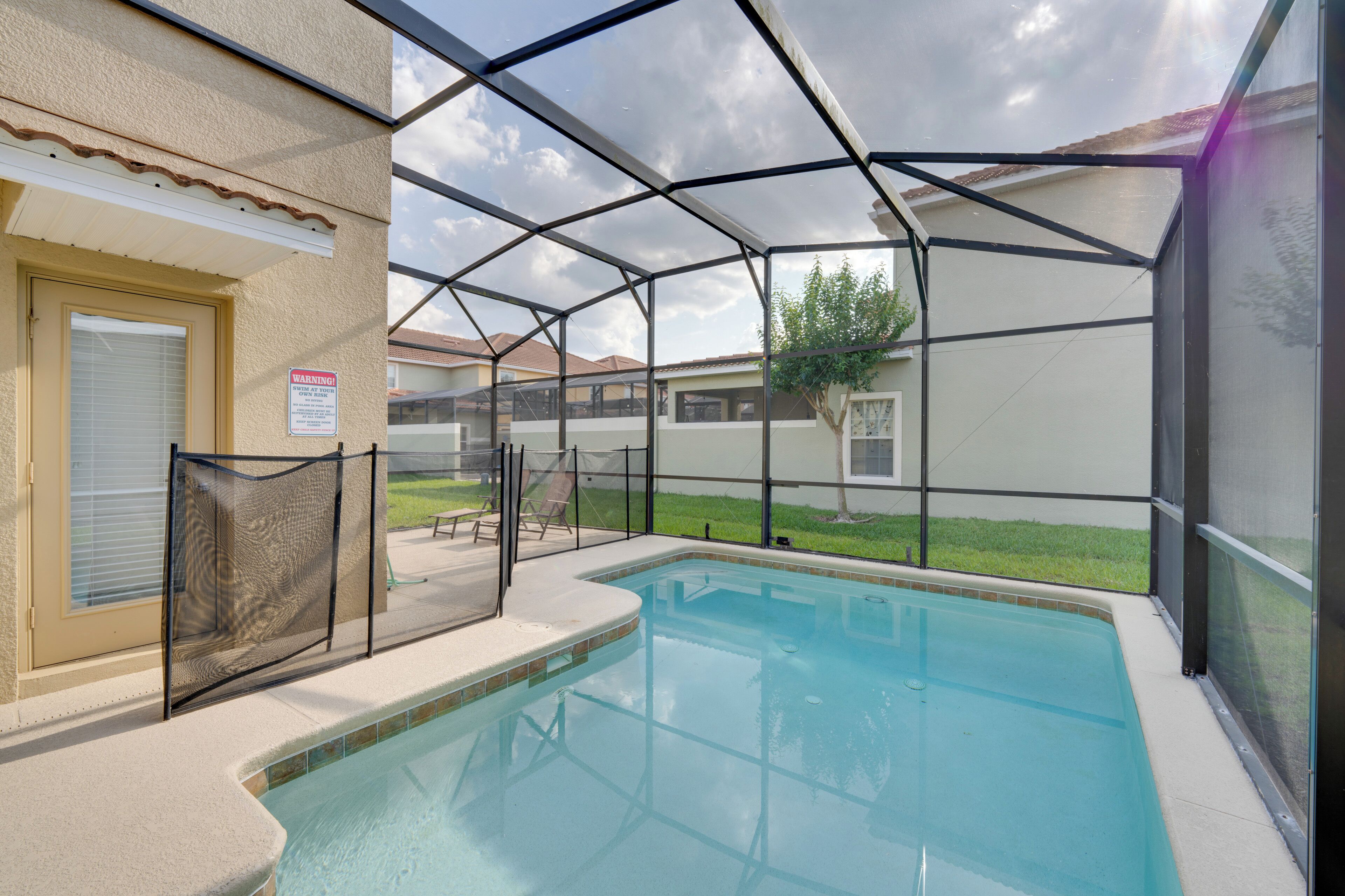 Ein überdachter Swimmingpool mit Sicherheitszaun, einer Tür und Blick auf eine Wohngegend im Hintergrund.