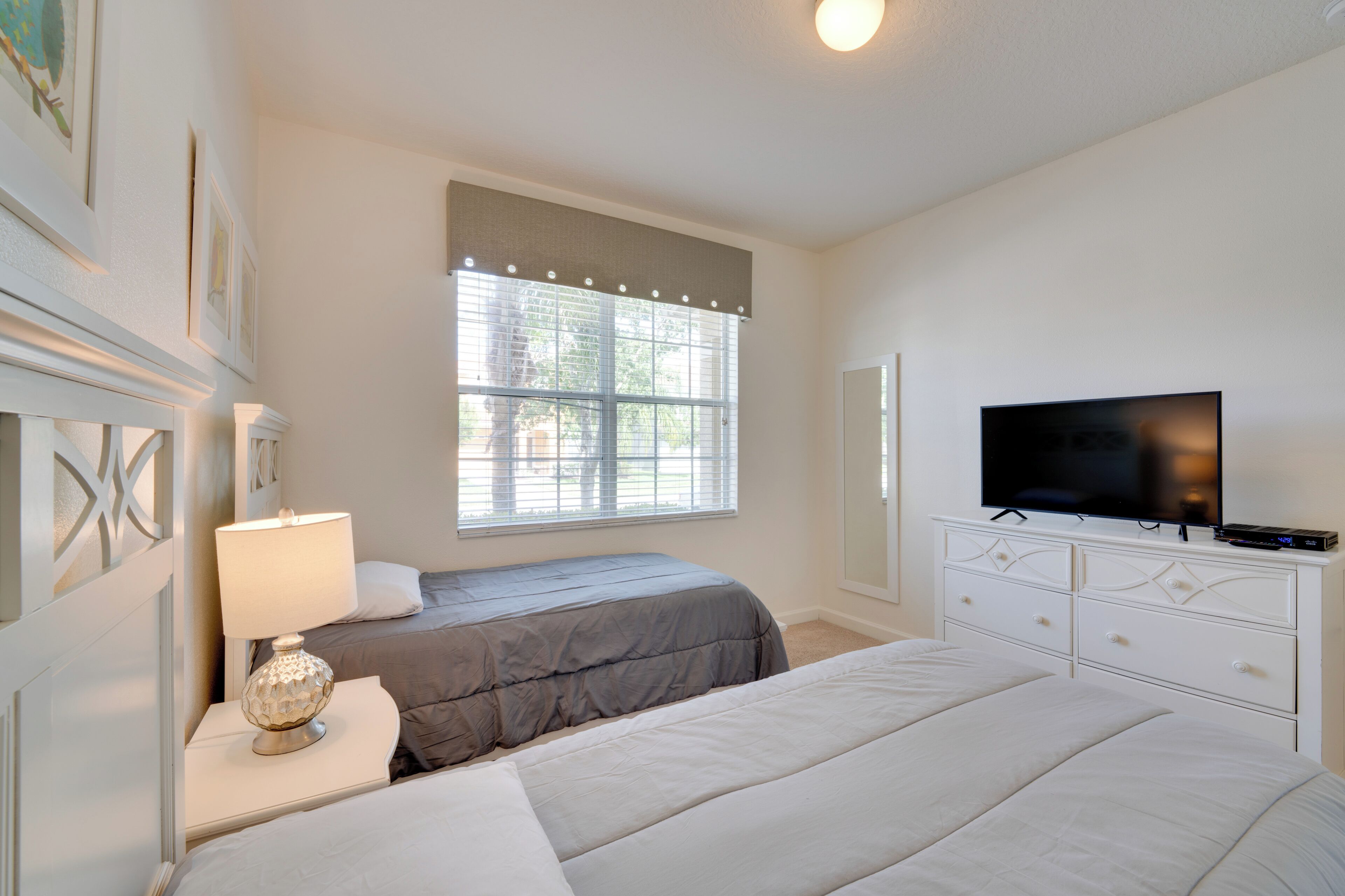 A bedroom with two beds, a TV, a lamp, and a window with blinds.