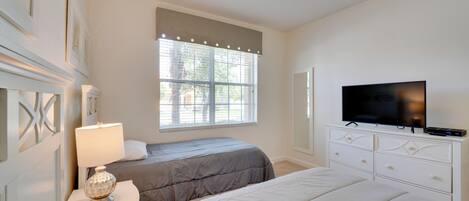 A bedroom with two beds, a TV, a lamp, and a window with blinds.