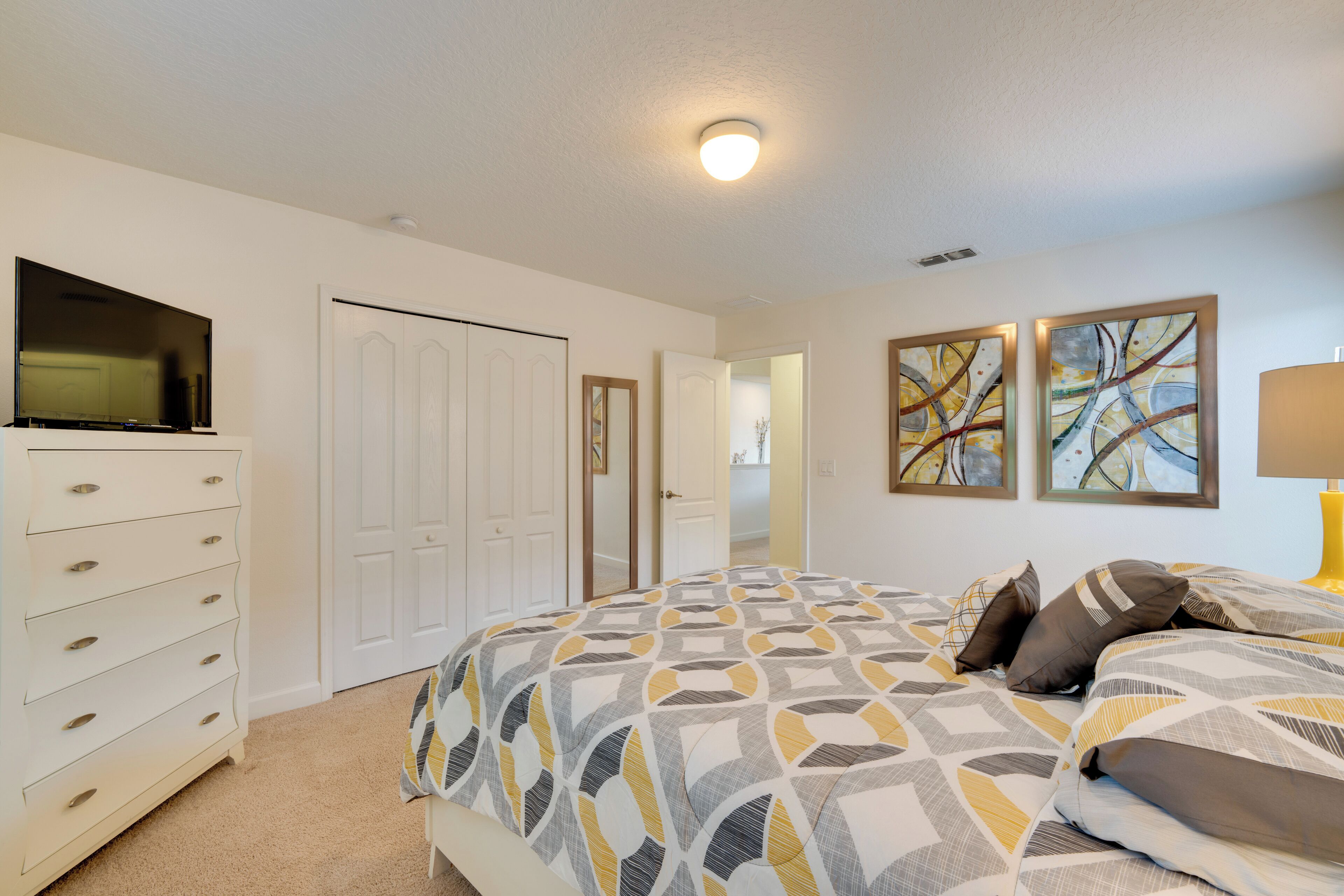 A bedroom with a bed, a dresser, a television, and two paintings on the wall.