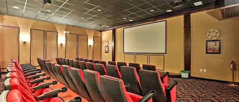 Sala de conferência com fileiras de cadeiras, um projetor e uma tela.
