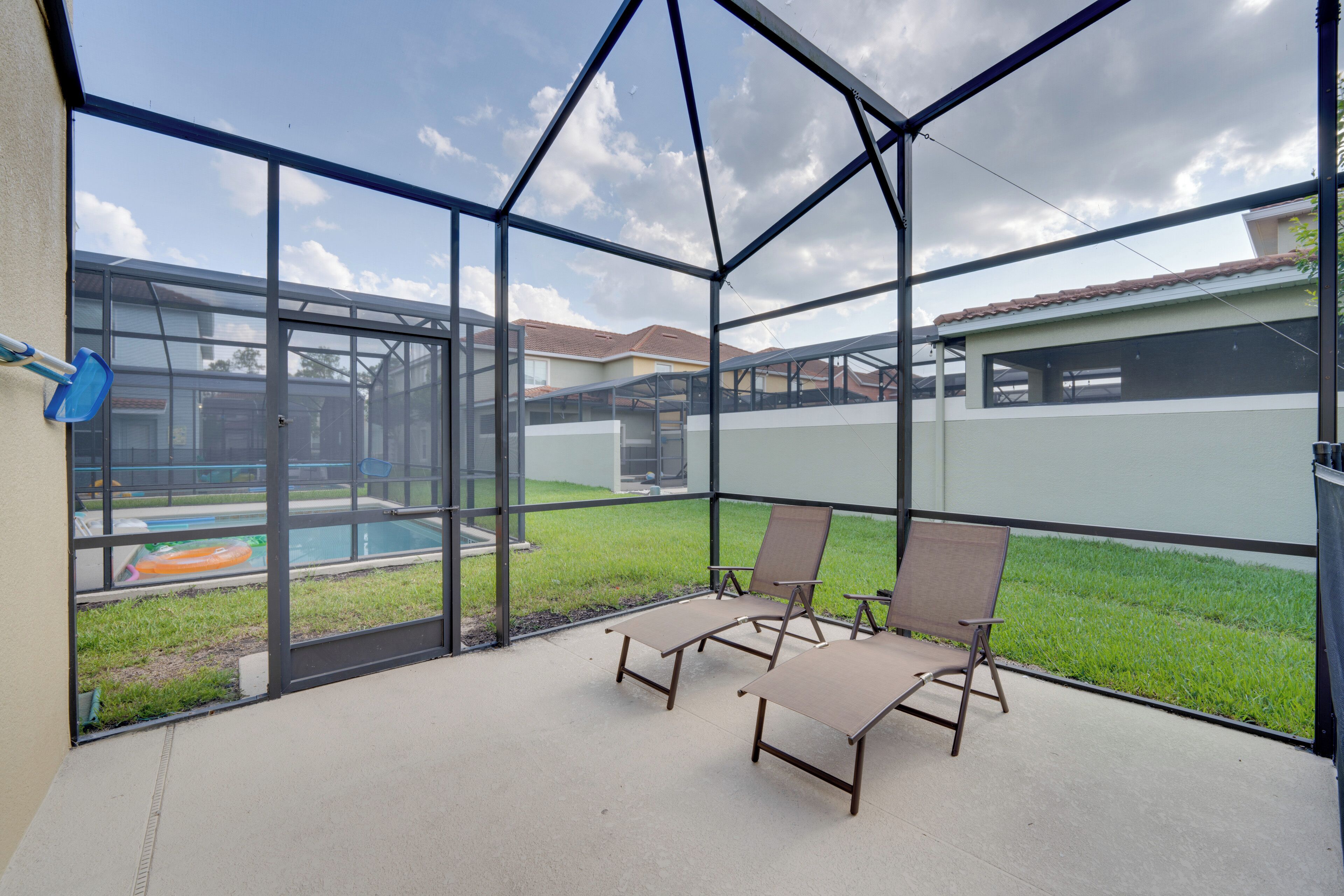 Un espace extérieur abrité, doté de murs en verre, de deux fauteuils et d’une piscine en arrière-plan.
