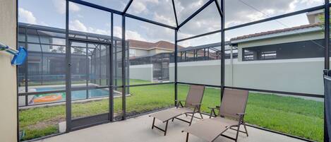 Un espace extérieur abrité, doté de murs en verre, de deux fauteuils et d’une piscine en arrière-plan.