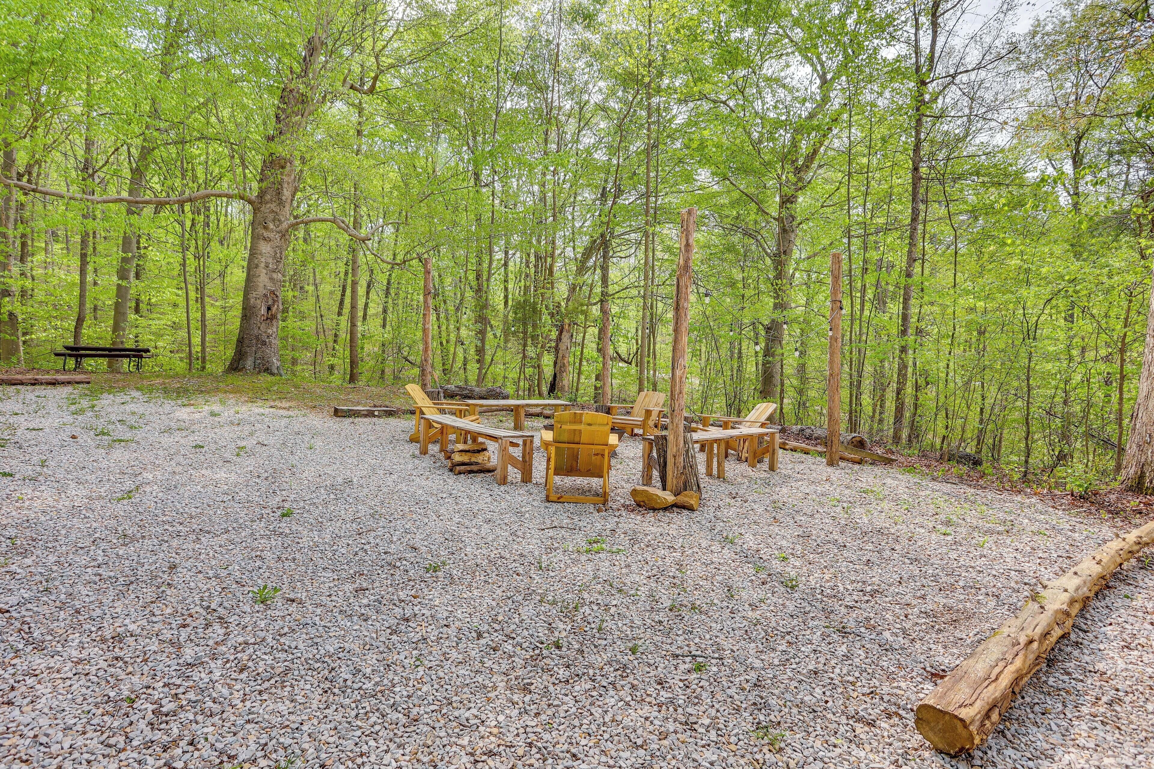 A forested area with a gravel ground and wooden picnic tables and chairs.