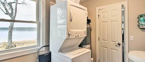 A laundry area with stacked washers and dryers, a window with a view of a tree and water, and a door to another room.
