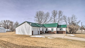 A single-story house with a green roof and white siding, located in a grassy area with bare trees in the background. - Pet-friendly Malta Home Near Hunting Areas! (Malta)