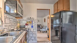 A kitchen with a stainless steel refrigerator, a microwave, and a stove. There is a sink and a countertop with a patterned backsplash. A chair and a couch are visible in the background. - Pet-friendly Malta Home Near Hunting Areas! (Malta)