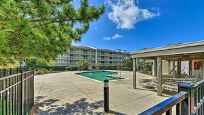 A pool area with a building in the background. - Point Emerald Resort Retreat: Walk to Beach! (Emerald Isle)