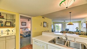 A kitchen with a dishwasher, double sink, and a dining area with a floral tablecloth. - Point Emerald Resort Retreat: Walk to Beach! (Emerald Isle)