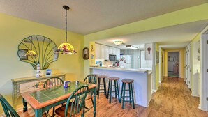 A dining area with a green table and chairs, a kitchen in the background, and a hallway leading to another room. - Point Emerald Resort Retreat: Walk to Beach! (Emerald Isle)
