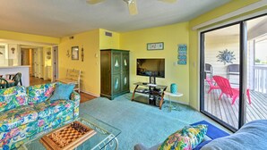 A living room with a ceiling fan, a TV, a chessboard, and a sliding glass door to a deck. - Point Emerald Resort Retreat: Walk to Beach! (Emerald Isle)