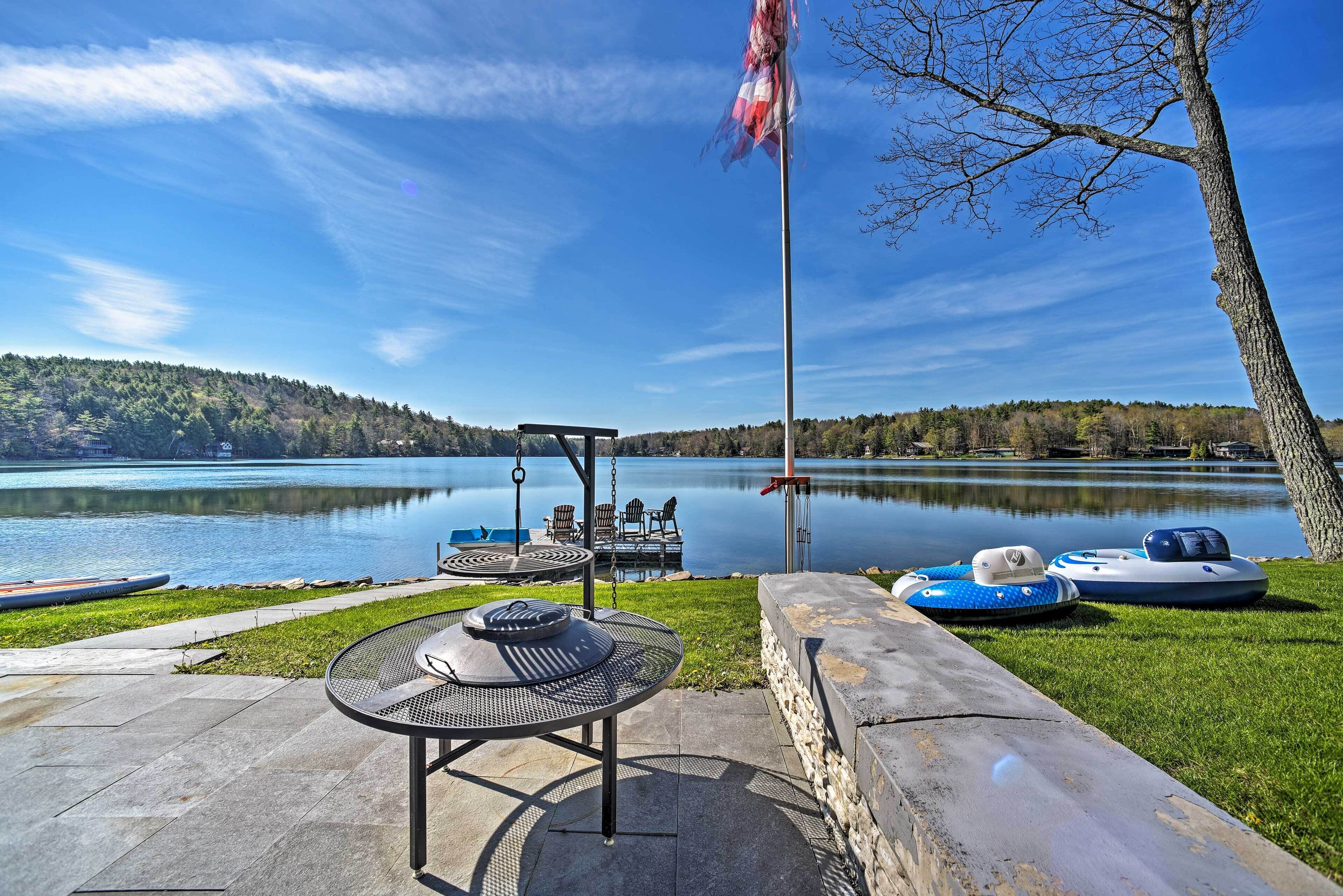 A lakeside patio with a table, chairs, and a flagpole.