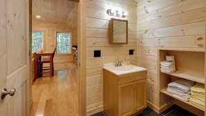 A wooden-paneled bathroom with a sink, mirror, and shelves with towels. - Cozy Apt w/ Deck, ~ 5 Miles to Acadia Nat'l Park! (Northeast Harbor)
