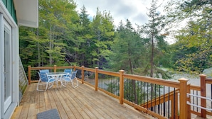 A wooden deck with a table and chairs, surrounded by a railing and dense forest. - Cozy Apt w/ Deck, ~ 5 Miles to Acadia Nat'l Park! (Northeast Harbor)