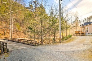 A gravel driveway leading to a wooden bridge over a stream, surrounded by trees and a house with a deck. - Idyllic Creekside Bryson City Gem w/ Fire Pit! (Bryson City)