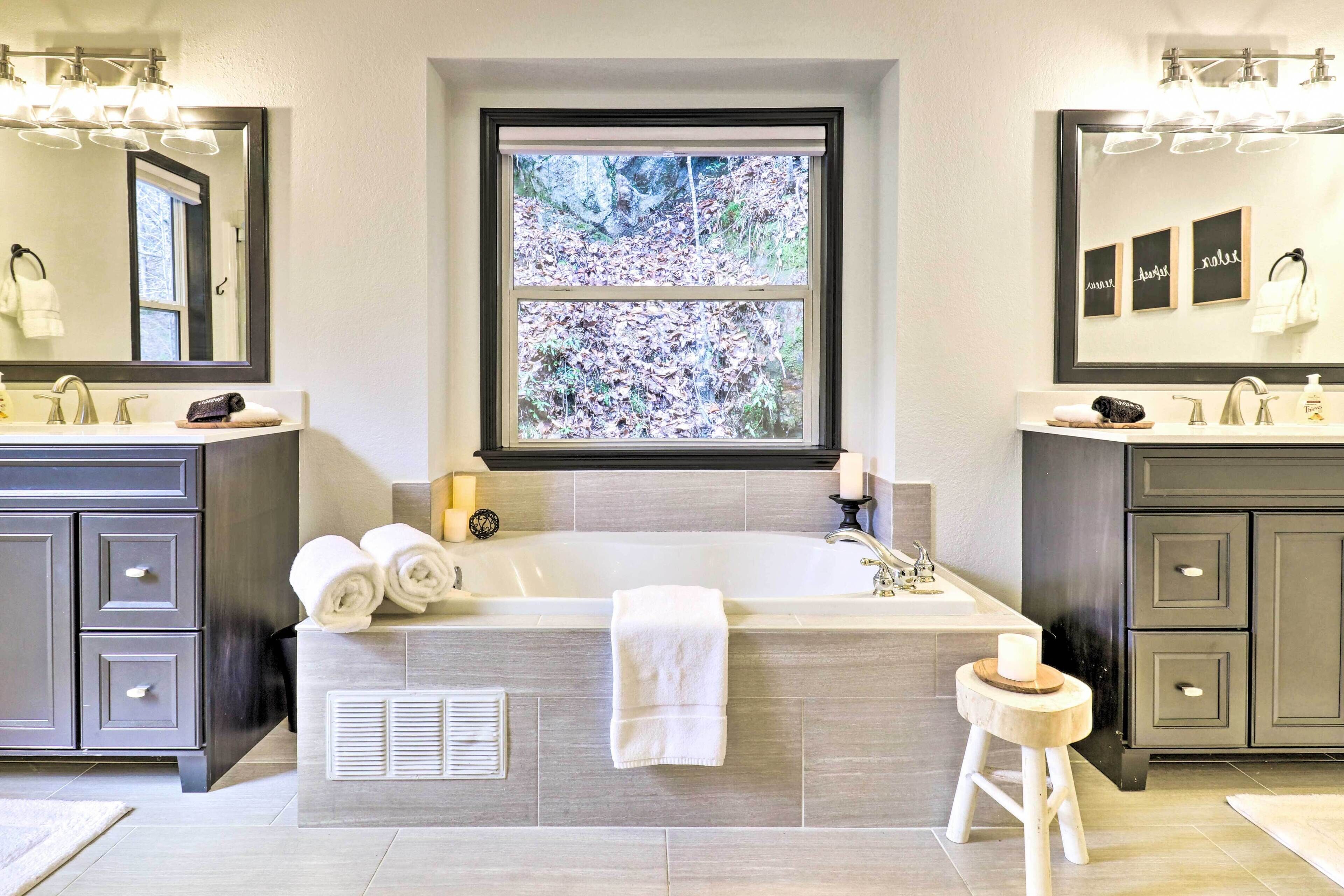 Un baño moderno con una bañera grande, dos lavamanos y un ventanal con vistas a la vegetación.