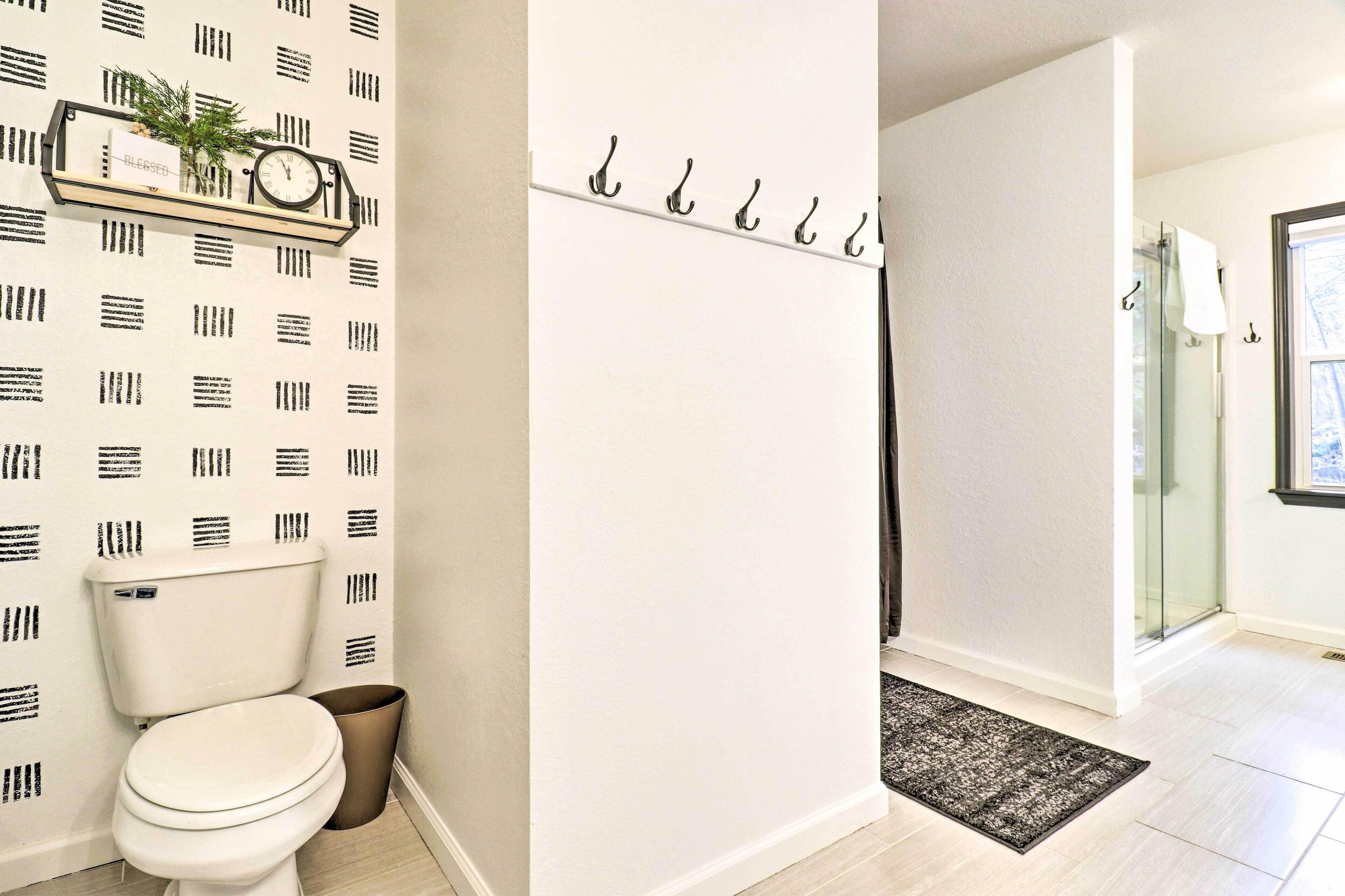Un baño con inodoro, estante con reloj y planta, zona de ducha y puerta de vidrio que da a la ducha.