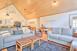 A spacious living room with a high ceiling, two sofas, a wooden coffee table, and a dining area in the background. - Idyllic Creekside Bryson City Gem w/ Fire Pit! (Bryson City)