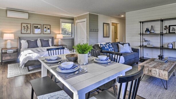 A modern, well-lit living room with a dining area, a sofa, and a coffee table. There are framed pictures on the wall, a plant on the coffee table, and a bookshelf with various items. - Scenic Studio w/ Loft & View of the Columbia River (Carson)