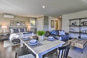 A modern, well-lit living room with a dining area, a sofa, and a coffee table. There are framed pictures on the wall, a plant on the coffee table, and a bookshelf with various items. - Scenic Studio w/ Loft & View of the Columbia River (Carson)