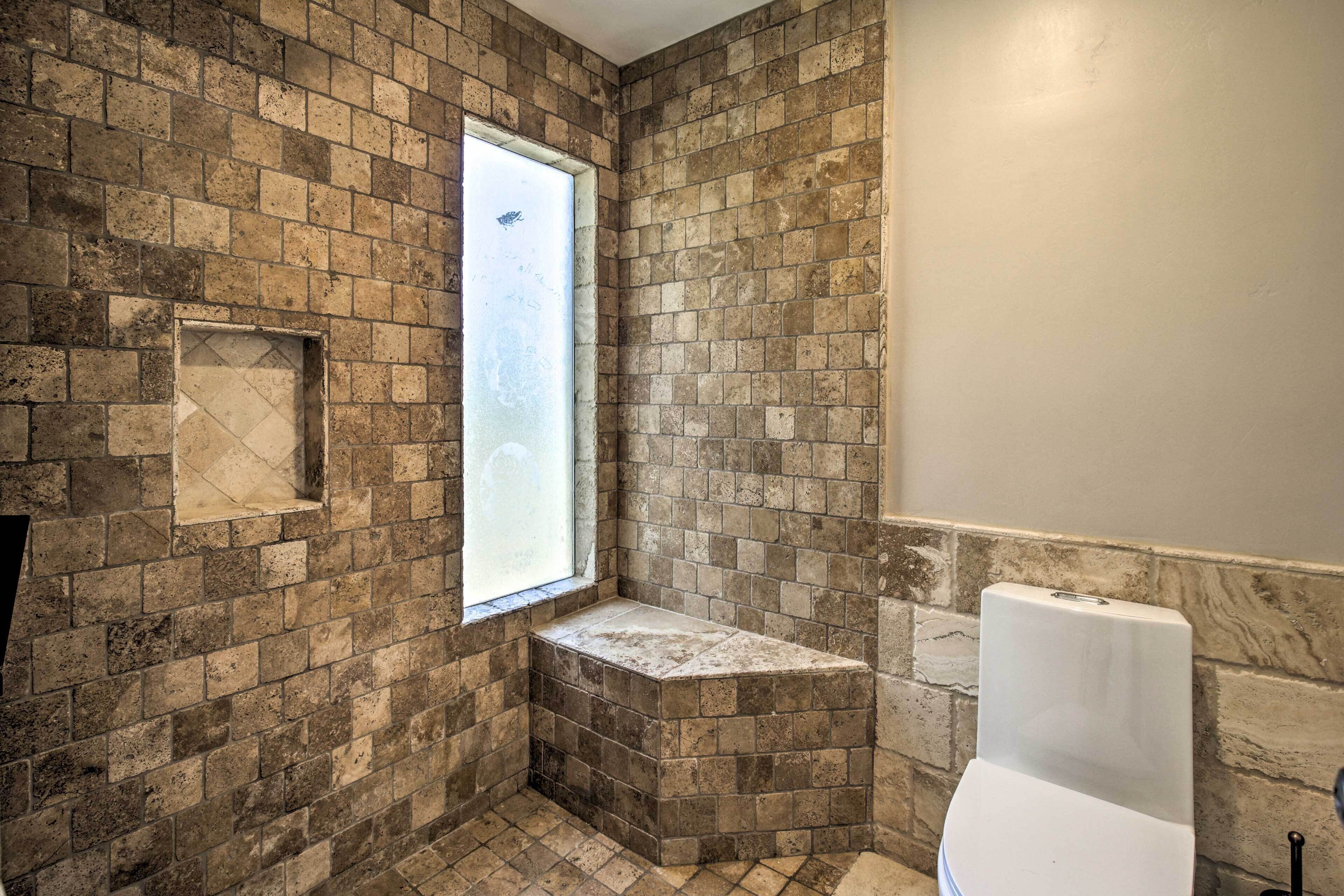 A bathroom with a stone wall, a window, and a toilet.